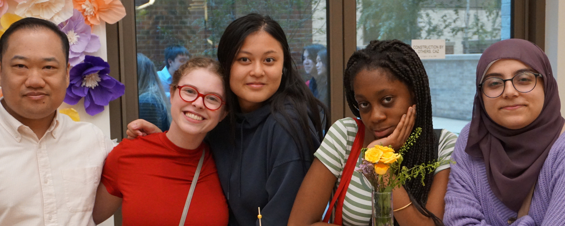A group of alumni and current students smiling and posing together in a school hallway.