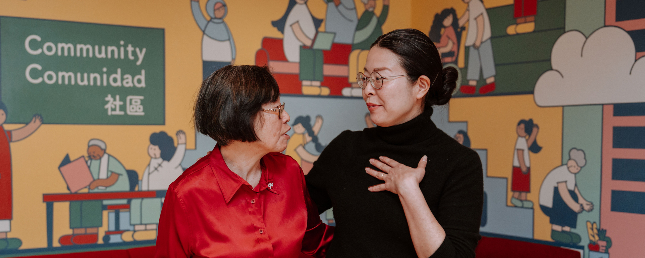 Two women talking warmly in front of a mural with the word community.