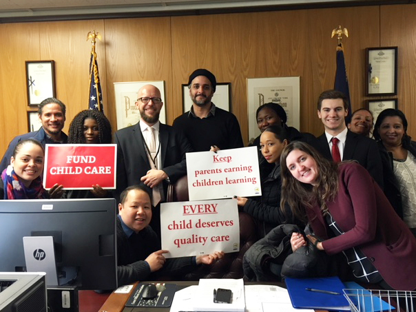 Henry Kam holds a "EVERY child deserves quality care" sign in Senator Peralta's office in Albany.