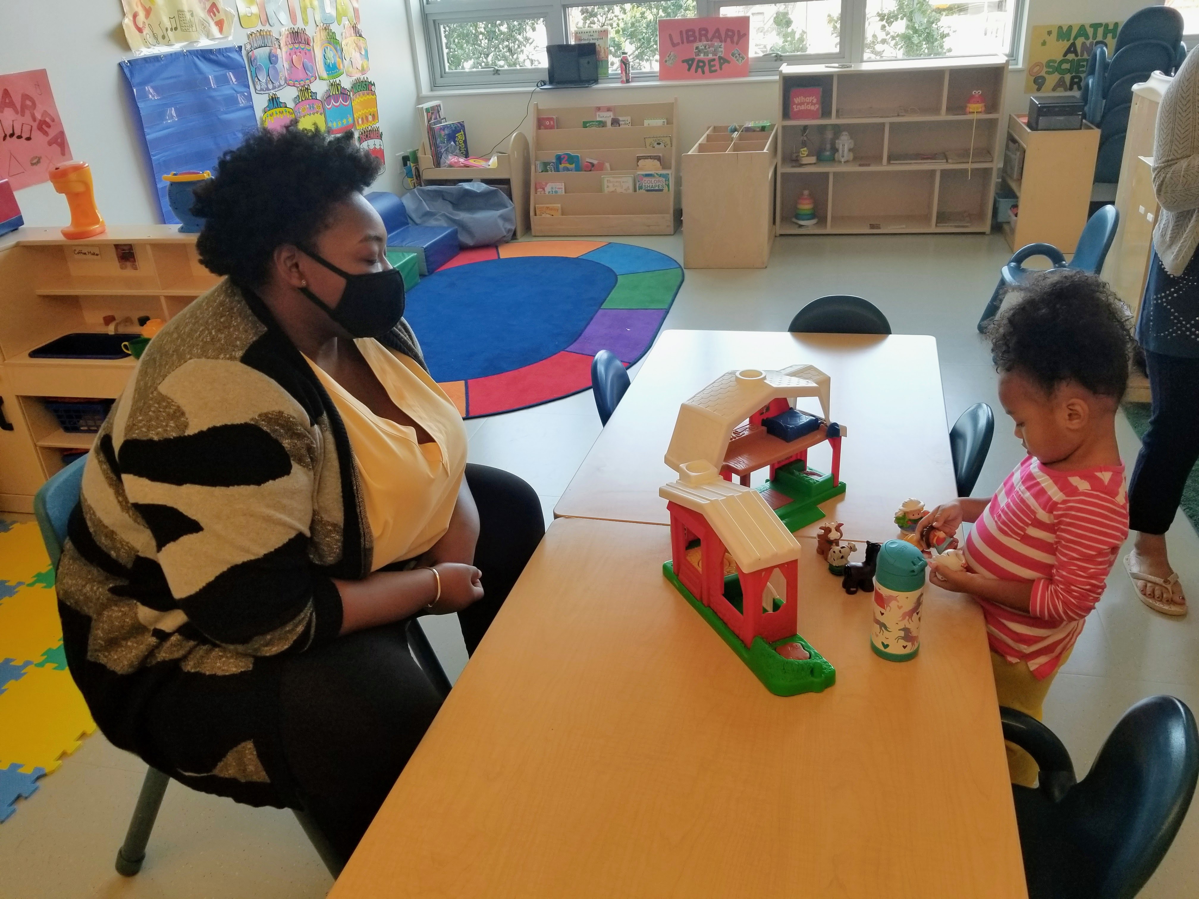 Staff wearing mask sit across a table from a child playing with blocks