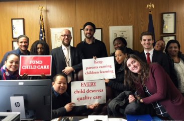 Henry Kam holds a "EVERY child deserves quality care" sign in Senator Peralta's office in Albany.