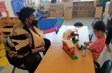 Staff wearing mask sit across a table from a child playing with blocks